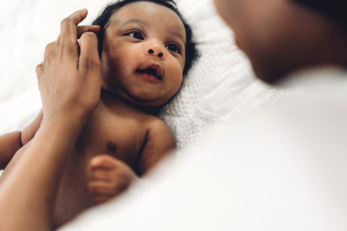 African american mother playing with adorable little african american baby in a white bedroom.Love of black family concept