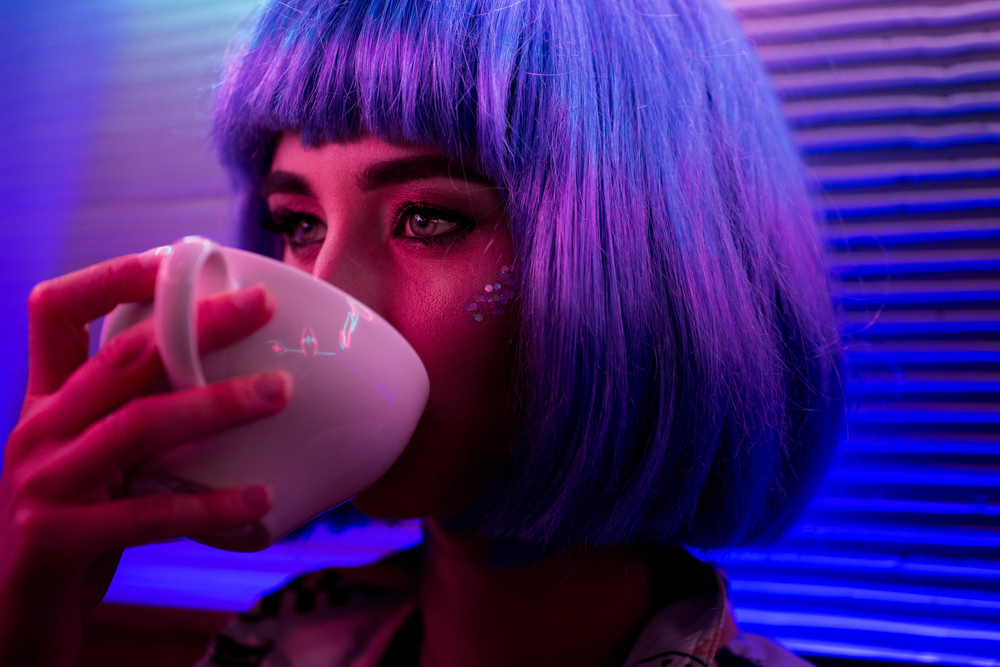 girl in a violet wig is drinking from a white cup