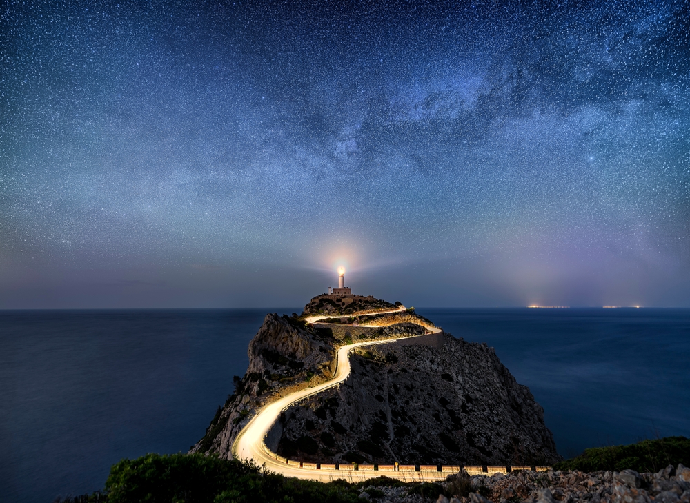 Light trails leading to a light house under the stars