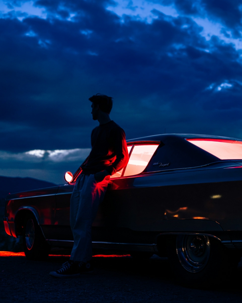 man in black leaning on a red car