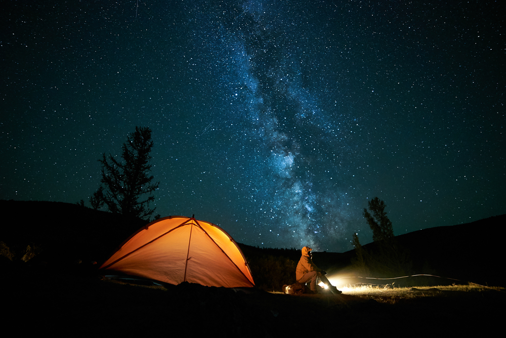 Man in orange coat by an orange tent under the Milky Way