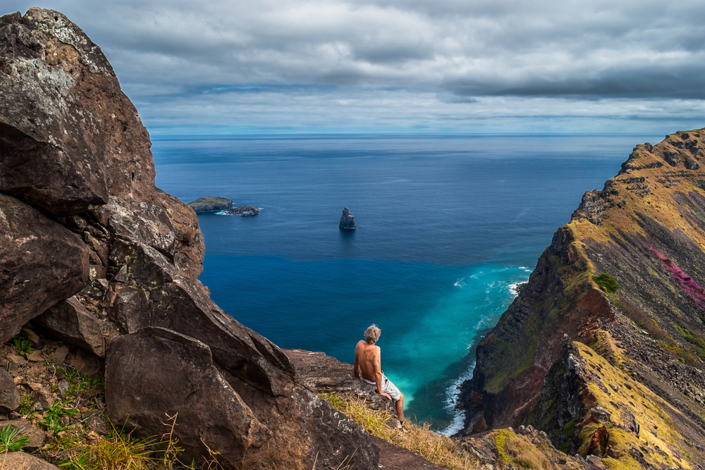 Man sitting on a cliff looking out over the sea at the rim of the crater of Rano Kao, Easter Island, Chile
