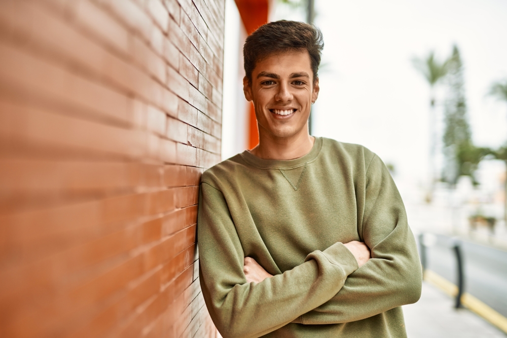man smiling with his arms crossed leaning against a wall