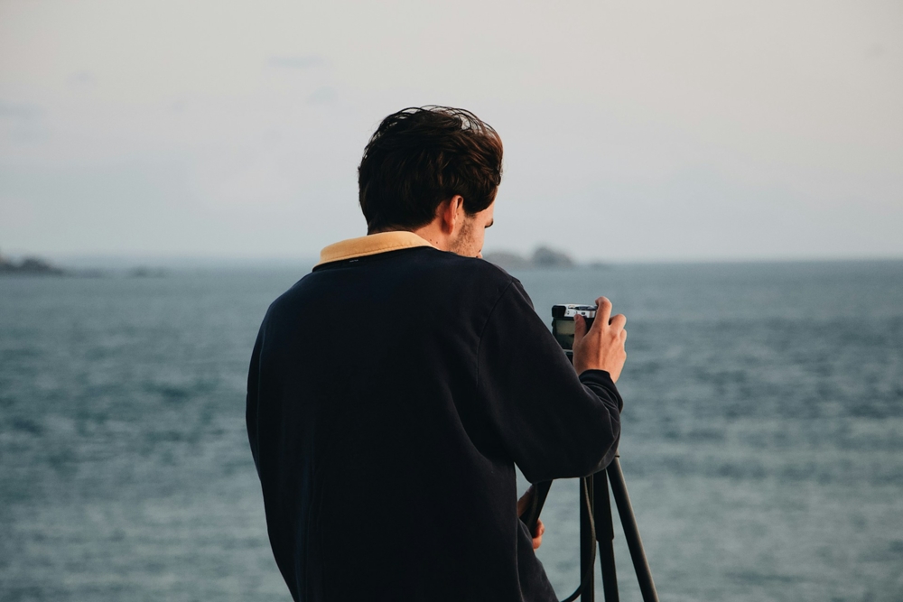 Man using a camera and tripod at the ocean