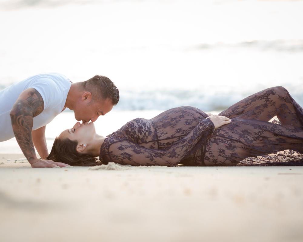 Maternity Photography mother laying on the beach kissed by father