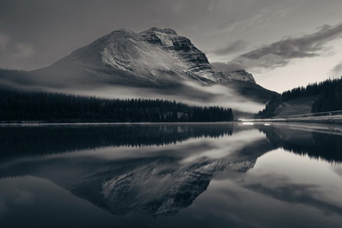 Mountain lake and traffic light trail with reflection and fog at sunset in Banff National Park, Canada.