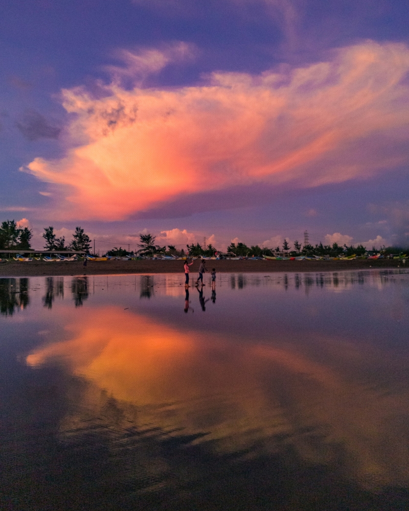 people standing by a lake under a cloudy sky with reflections