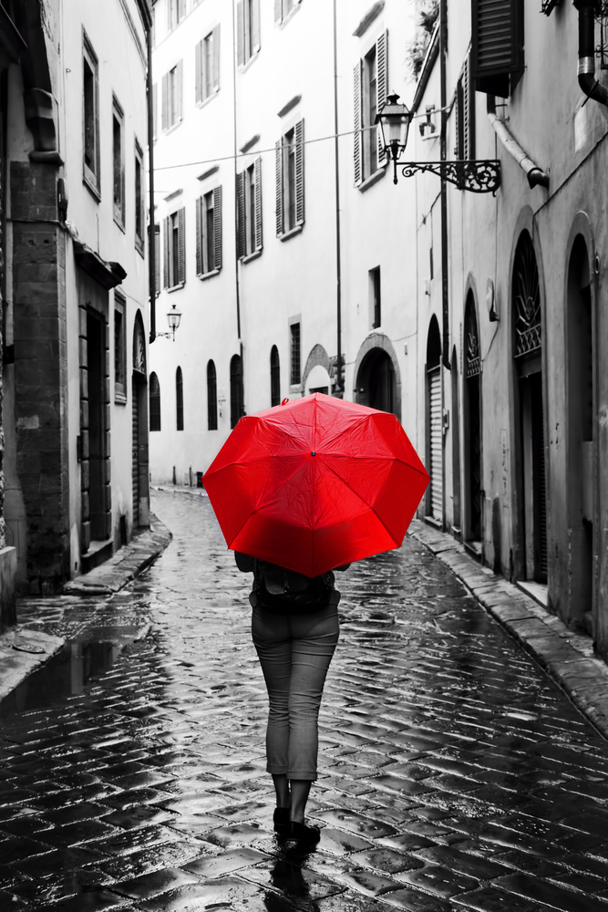 Woman with red umbrella on cobblestone street Black and white with spot color BW